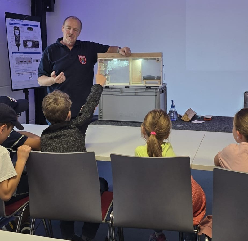 Der Ausbilder erklärt die Rauchausbreitung anhand eines Modells, dem sogenannten Rauchhaus